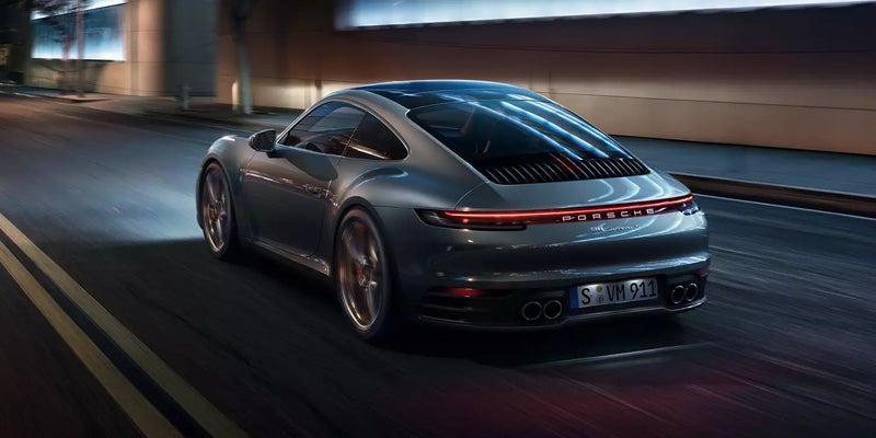Rear view of a silver 2024 Porsche 911 driving down a lit highway at night
