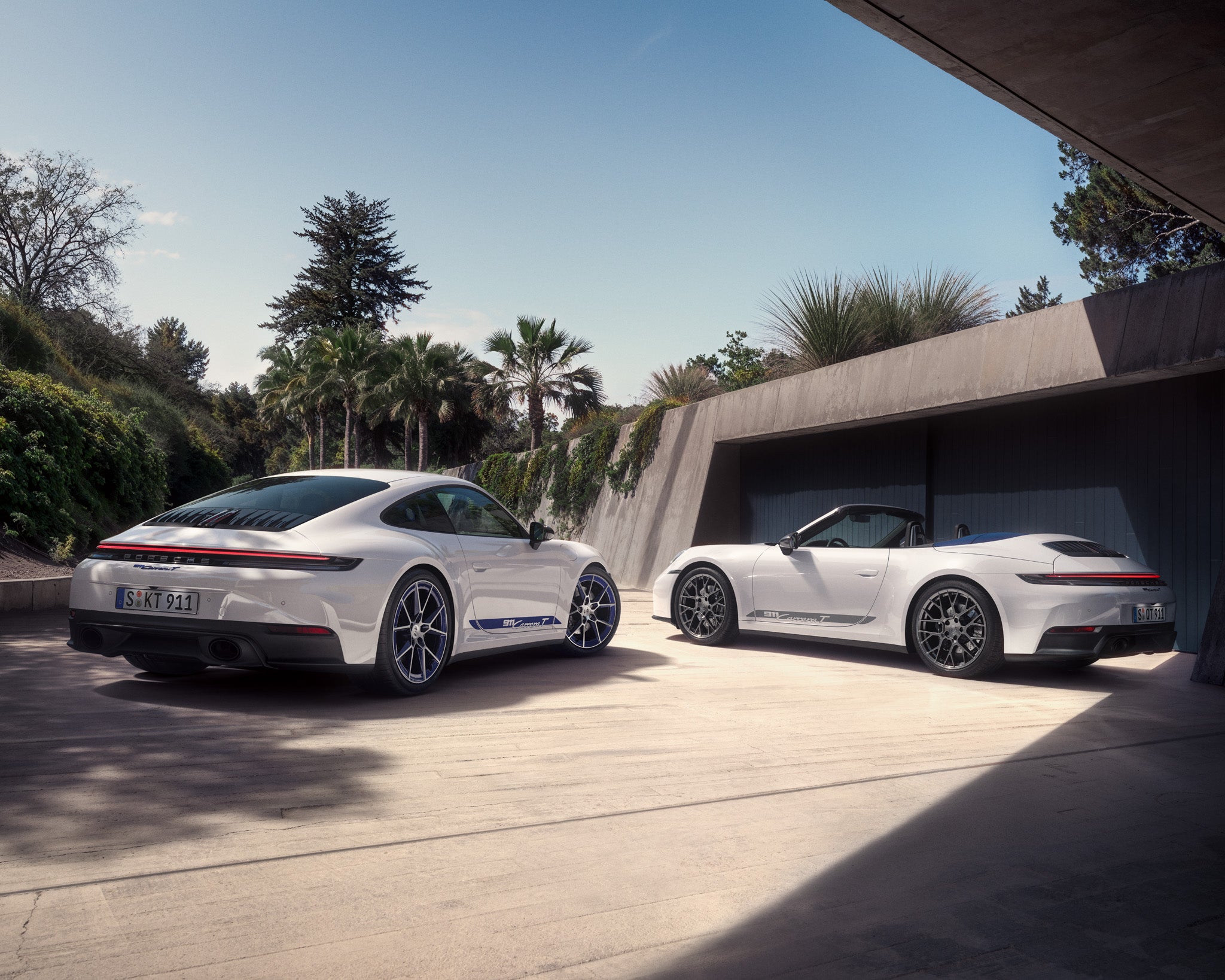 Two iconic white Porsche 911s side by side — a sleek coupe and an open-top convertible.