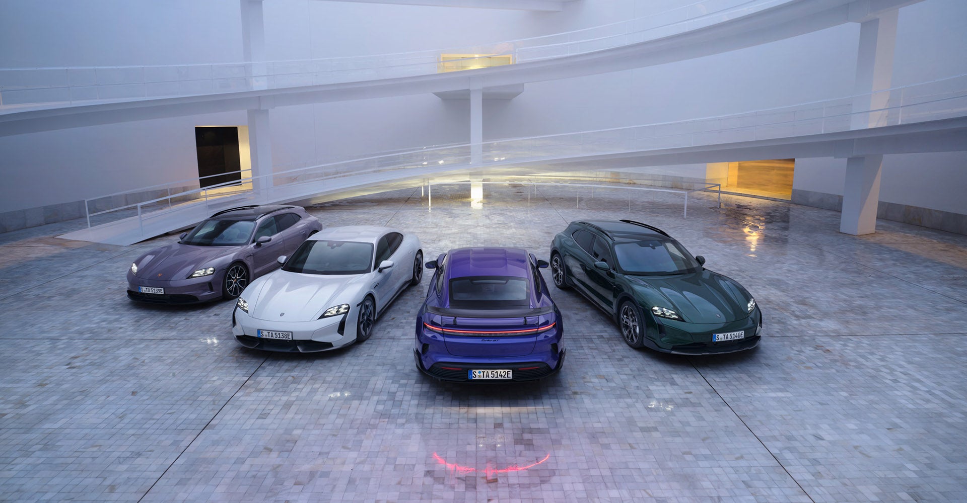 Four Porsche Taycan in different colors parked in an elegant space with smooth lighting.