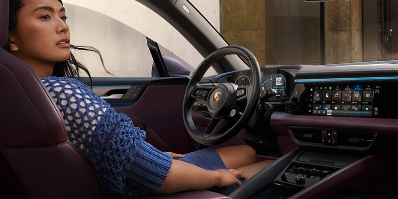 A woman looking to the right while behind the steering wheel of a 2025 Porsche Macan EV